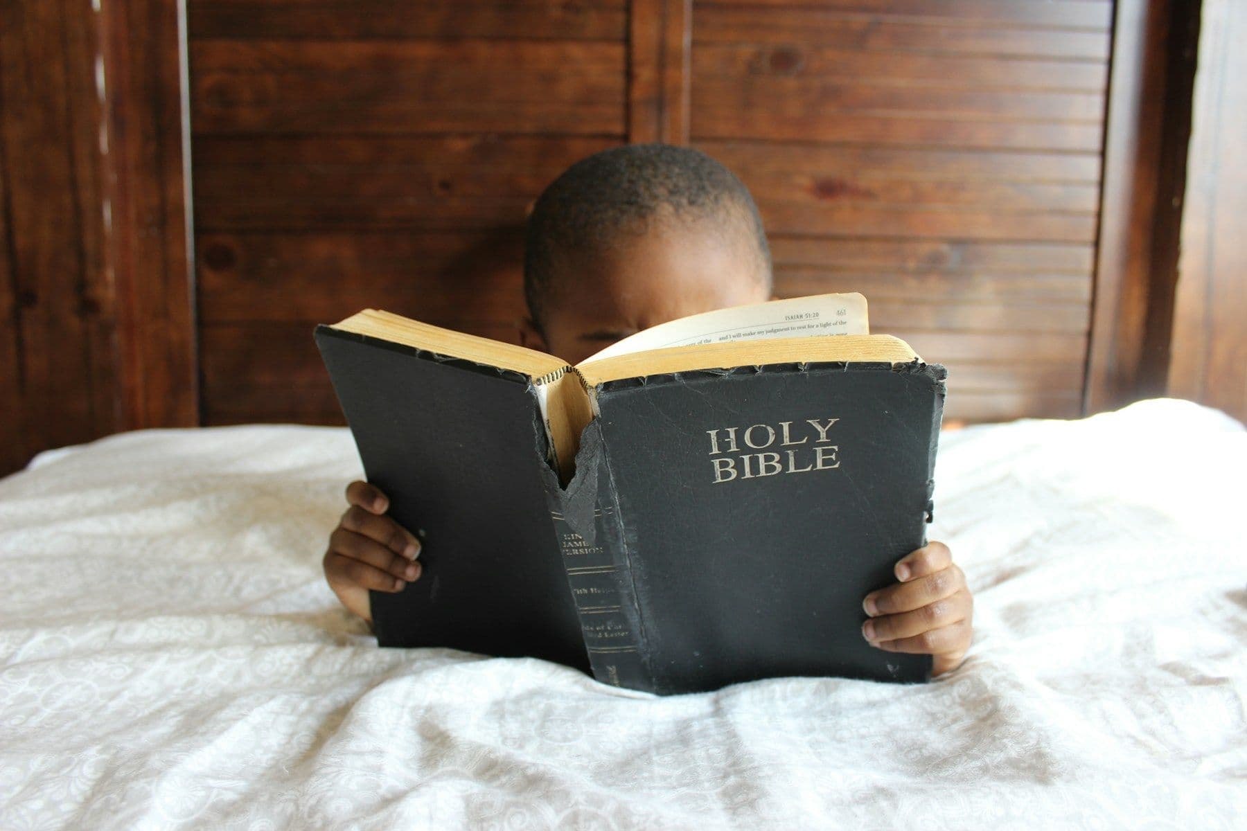 A young boy reading a Bible in bed