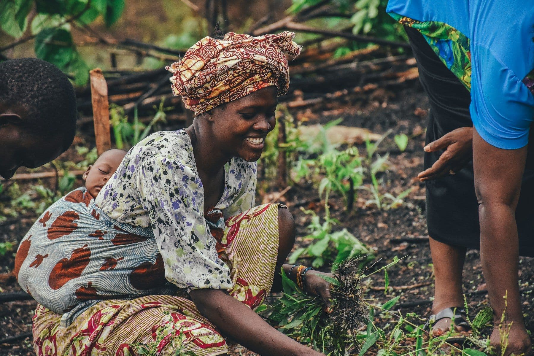 A smiling woman in a headwrap planting seedlings in a garden